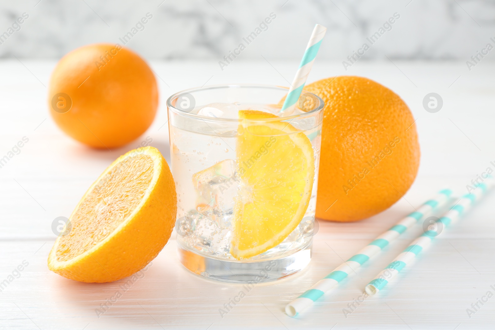 Photo of Sparkling water with orange slice in glass and fresh fruits on white wooden table, closeup
