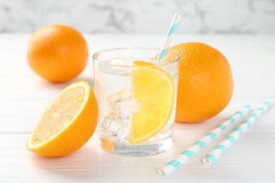 Photo of Sparkling water with orange slice in glass and fresh fruits on white wooden table, closeup