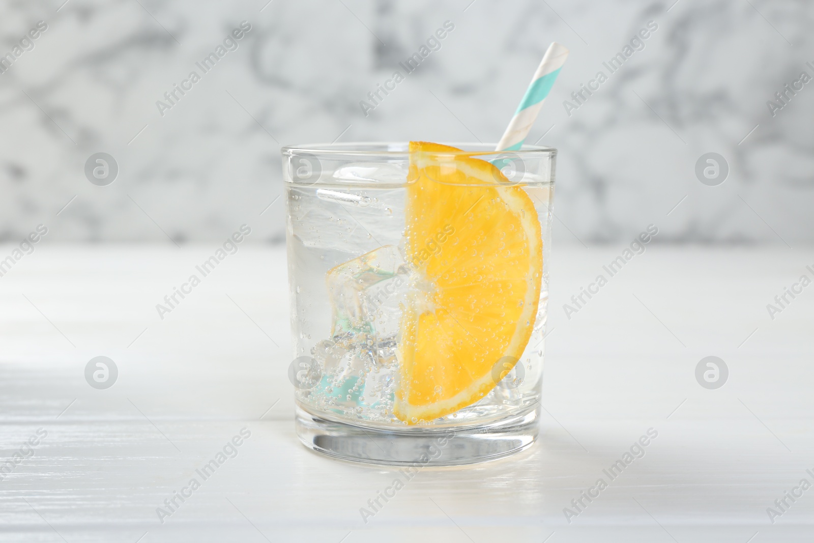 Photo of Sparkling water with orange slice in glass on white wooden table, closeup