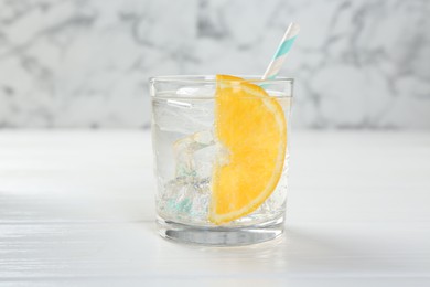 Photo of Sparkling water with orange slice in glass on white wooden table, closeup