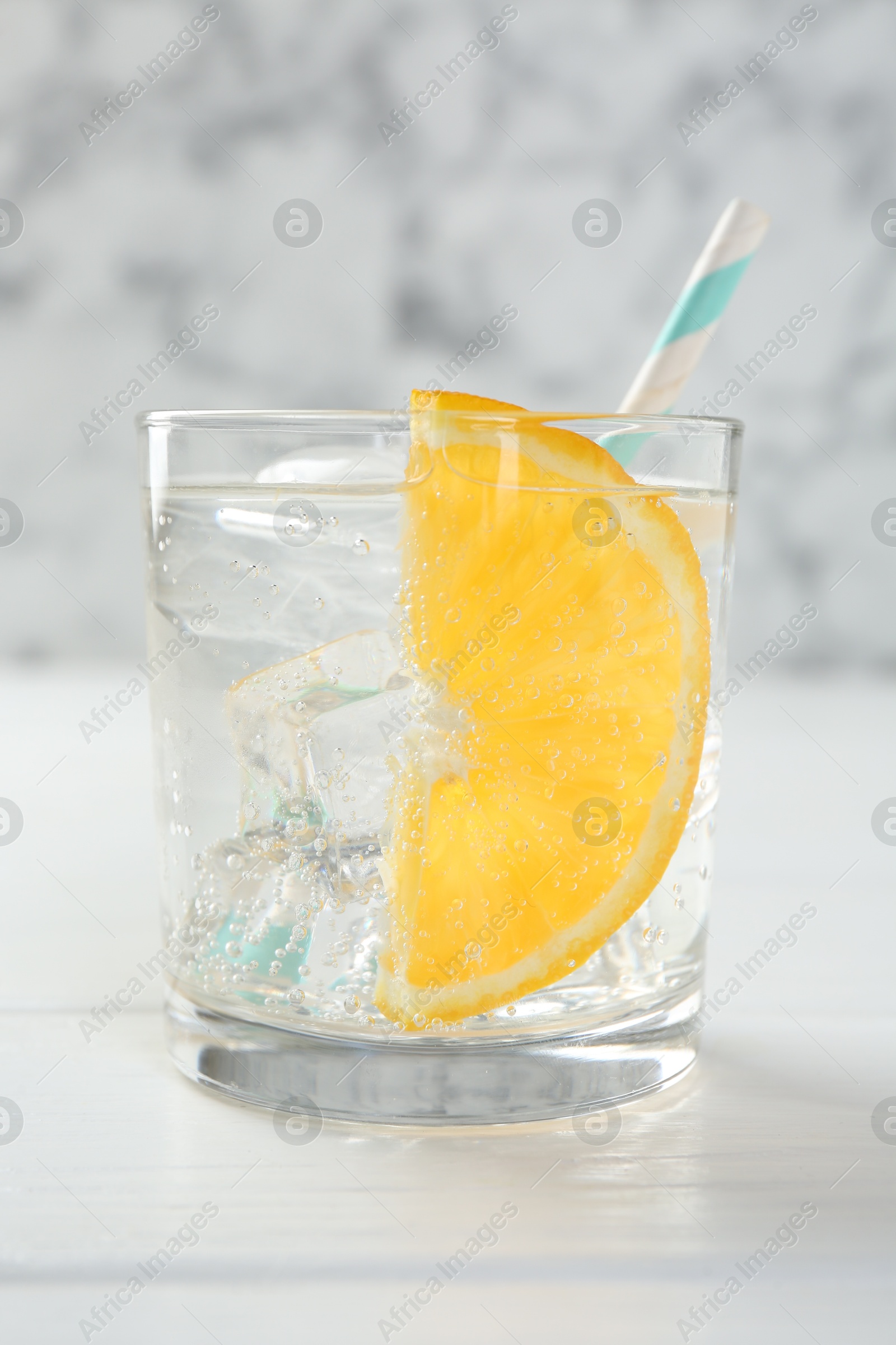 Photo of Sparkling water with orange slice in glass on white wooden table, closeup