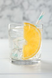 Photo of Sparkling water with orange slice in glass on white wooden table, closeup