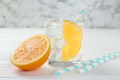 Photo of Sparkling water with orange slice in glass and fresh fruit on white wooden table, closeup