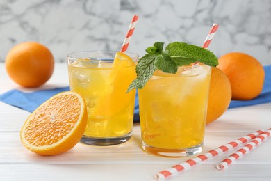 Photo of Refreshing soda water with orange slices in glasses, mint and fresh fruits on white wooden table, closeup