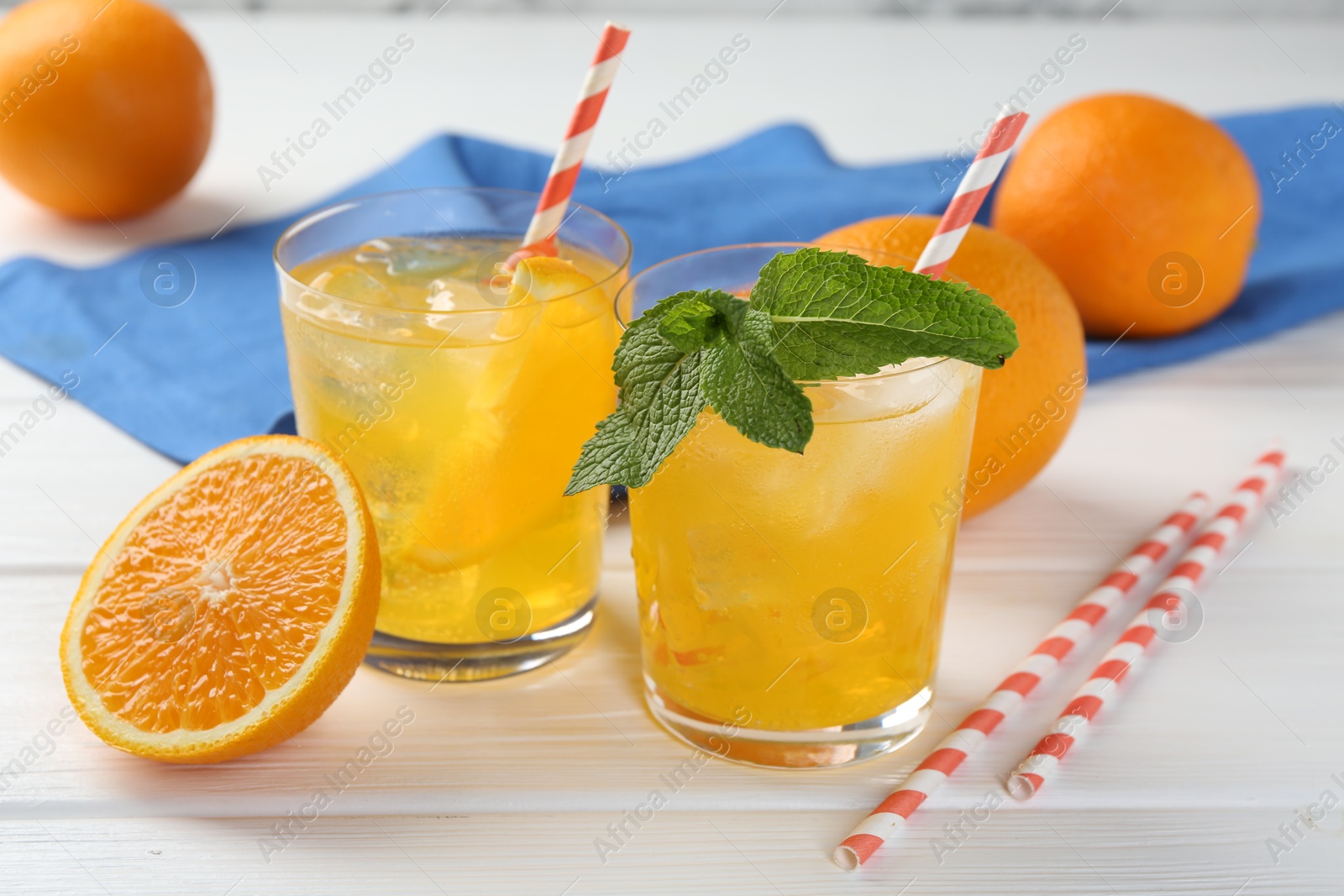 Photo of Refreshing soda water with orange slices in glasses, mint and fresh fruits on white wooden table, closeup