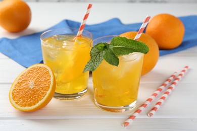Photo of Refreshing soda water with orange slices in glasses, mint and fresh fruits on white wooden table, closeup