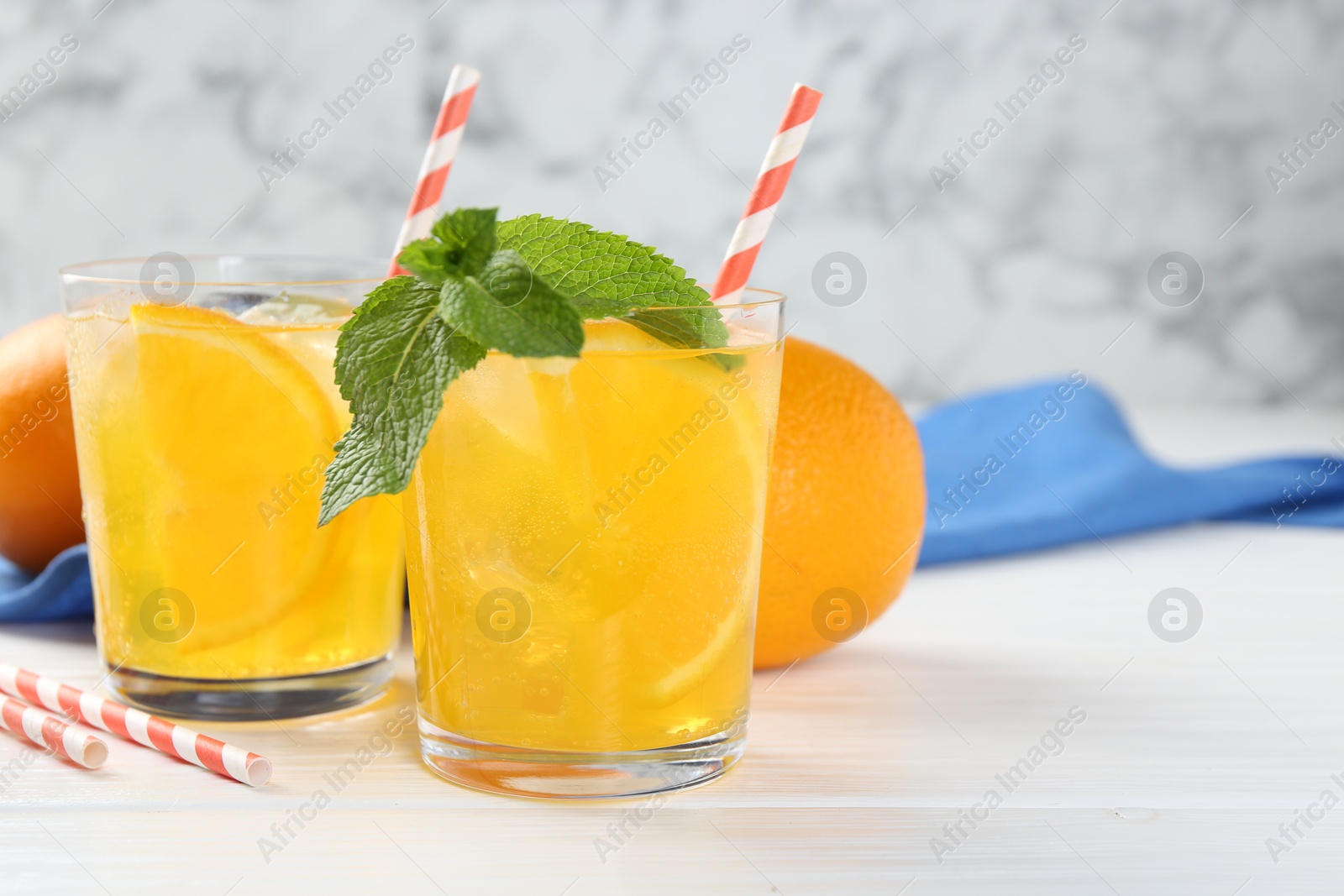 Photo of Refreshing soda water with orange slices in glasses, mint and fresh fruits on white wooden table, closeup