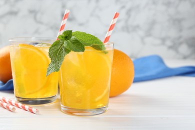 Photo of Refreshing soda water with orange slices in glasses, mint and fresh fruits on white wooden table, closeup