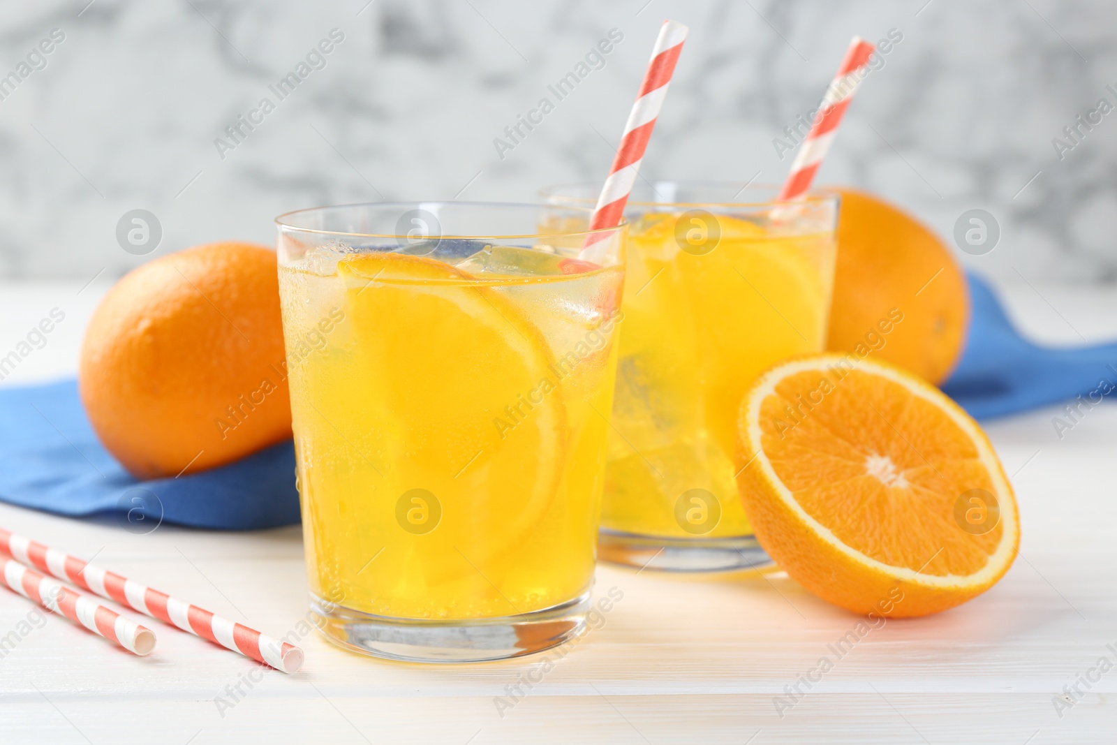 Photo of Refreshing soda water with orange slices in glasses and fresh fruits on white wooden table, closeup