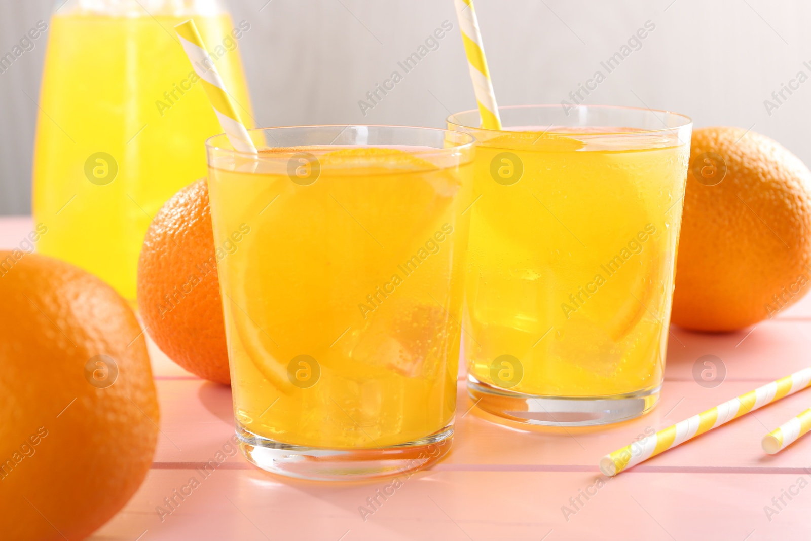 Photo of Refreshing soda water with orange slices in glasses, jug and fresh fruits on pink wooden table, closeup