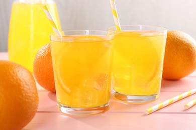 Photo of Refreshing soda water with orange slices in glasses, jug and fresh fruits on pink wooden table, closeup