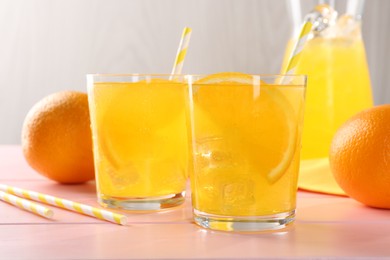 Photo of Refreshing soda water with orange slices in glasses, jug and fresh fruits on pink wooden table, closeup