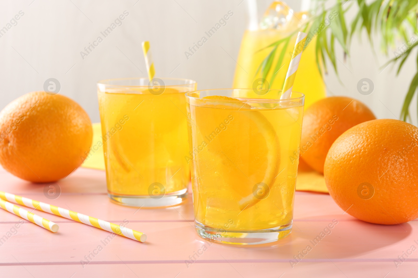 Photo of Refreshing soda water with orange slices in glasses, jug and fresh fruits on pink wooden table, closeup
