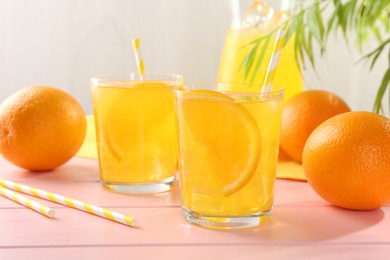Photo of Refreshing soda water with orange slices in glasses, jug and fresh fruits on pink wooden table, closeup