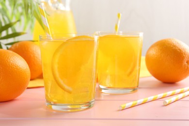 Photo of Refreshing soda water with orange slices in glasses, jug and fresh fruits on pink wooden table, closeup