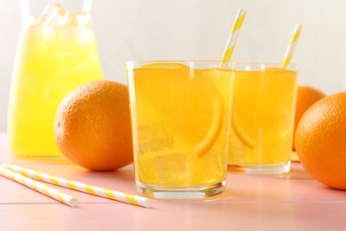 Photo of Refreshing soda water with orange slices in glasses, jug and fresh fruits on pink wooden table, closeup