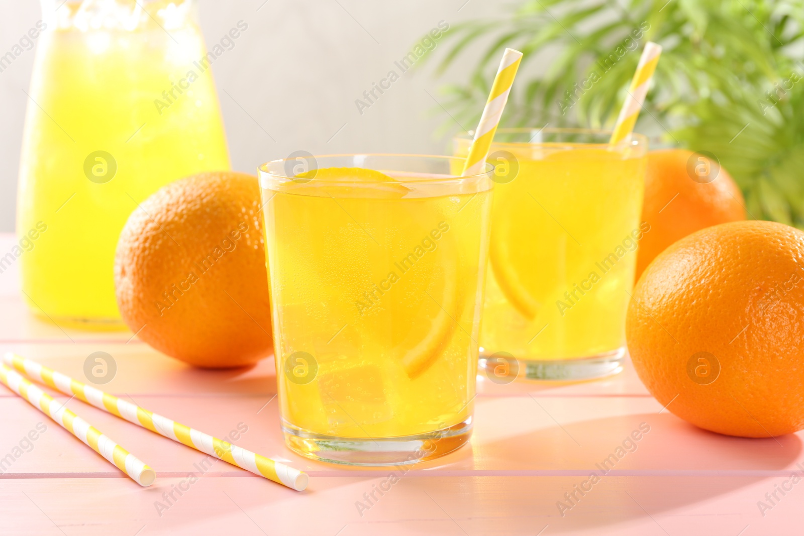Photo of Refreshing soda water with orange slices in glasses, jug and fresh fruits on pink wooden table, closeup