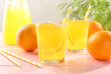 Photo of Refreshing soda water with orange slices in glasses, jug and fresh fruits on pink wooden table, closeup