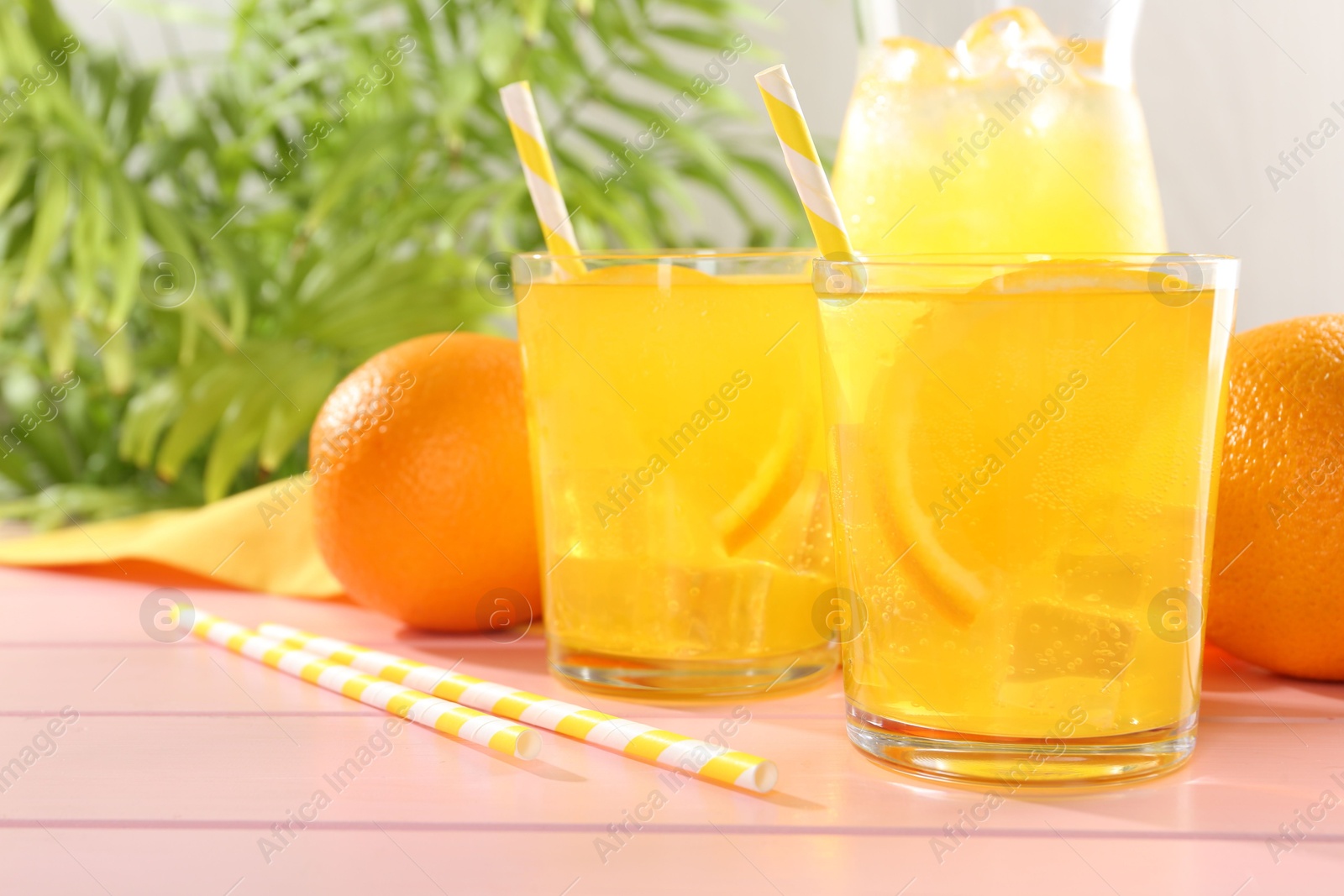 Photo of Refreshing soda water with orange slices in glasses, jug and fresh fruits on pink wooden table, closeup
