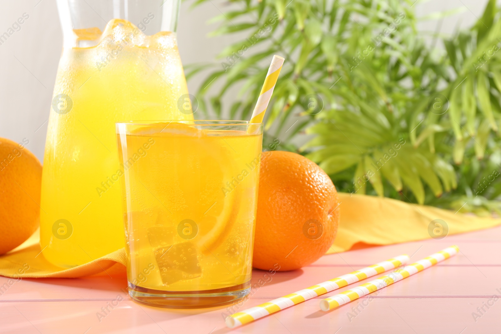 Photo of Refreshing soda water with orange slice in glass, jug and fresh fruits on pink wooden table, closeup