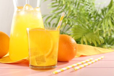 Photo of Refreshing soda water with orange slice in glass, jug and fresh fruits on pink wooden table, closeup