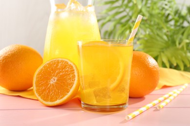Photo of Refreshing soda water with orange slice in glass, jug and fresh fruits on pink wooden table, closeup