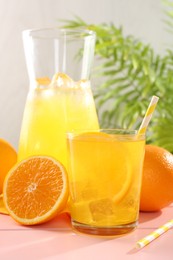 Photo of Refreshing soda water with orange slice in glass, jug and fresh fruits on pink wooden table, closeup