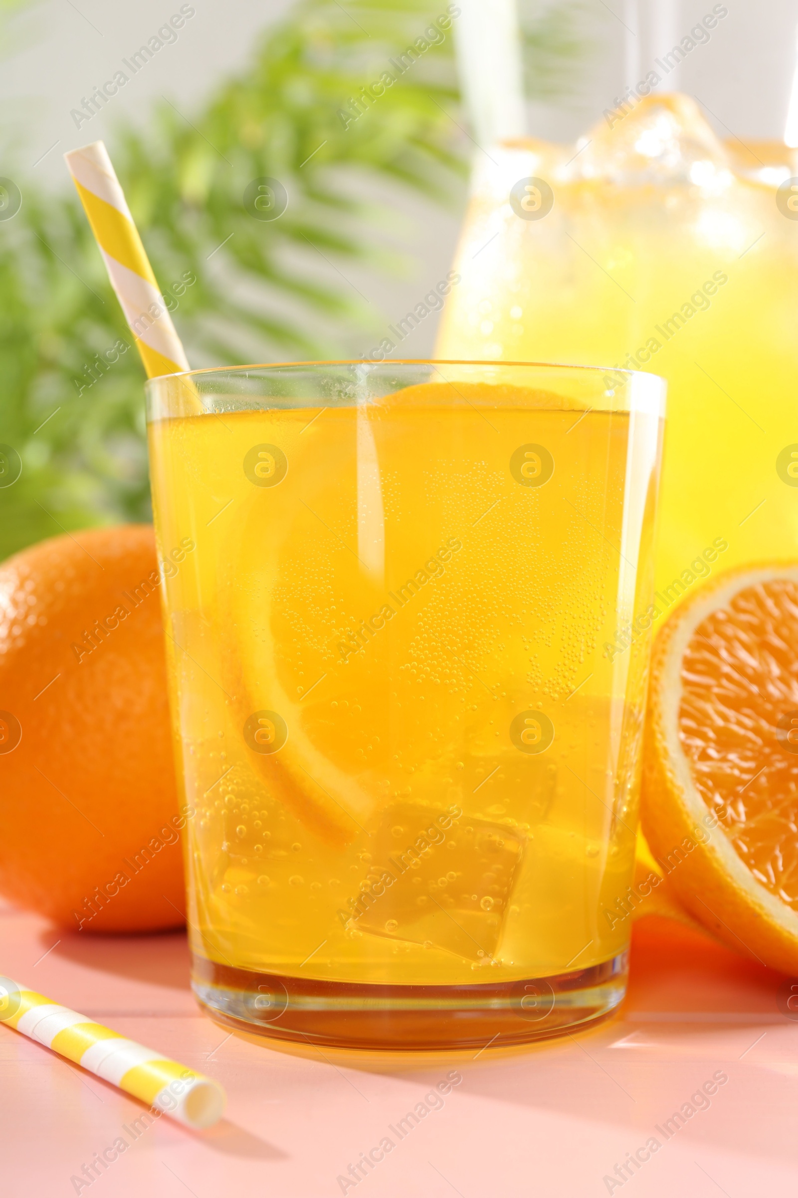 Photo of Refreshing soda water with orange slice in glass, jug and fresh fruits on pink wooden table, closeup