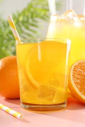 Photo of Refreshing soda water with orange slice in glass, jug and fresh fruits on pink wooden table, closeup