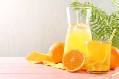 Photo of Refreshing soda water with orange slice in glass, jug and fresh fruits on pink wooden table, closeup