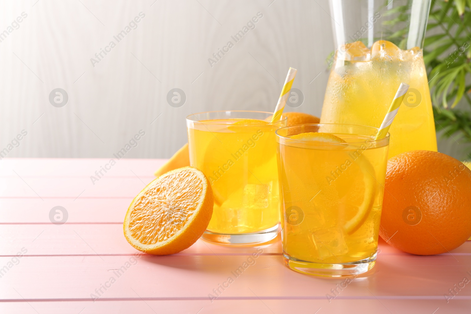Photo of Refreshing soda water with orange slices in glasses, jug and fresh fruits on pink wooden table, closeup