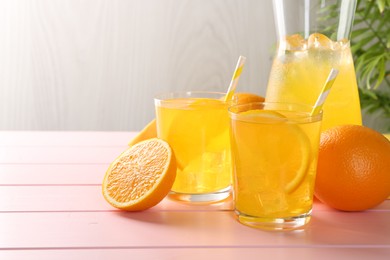 Photo of Refreshing soda water with orange slices in glasses, jug and fresh fruits on pink wooden table, closeup