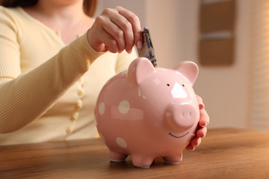 Photo of Woman putting money into piggybank at wooden table, closeup