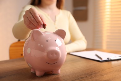 Photo of Woman putting money into piggybank at wooden table, closeup