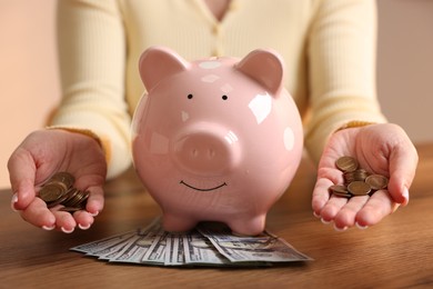 Photo of Woman with piggybank and money at wooden table, closeup