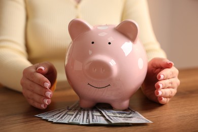 Photo of Woman with piggybank and money at wooden table, closeup