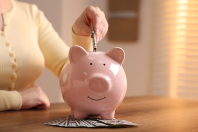 Photo of Woman putting money into piggybank at wooden table, closeup