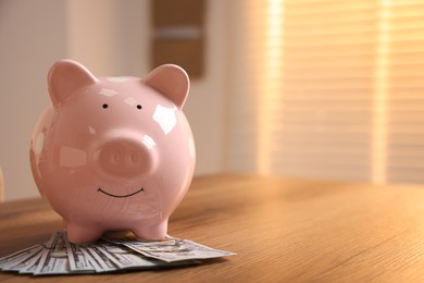Photo of Piggybank and dollar banknotes on wooden table. Space for text