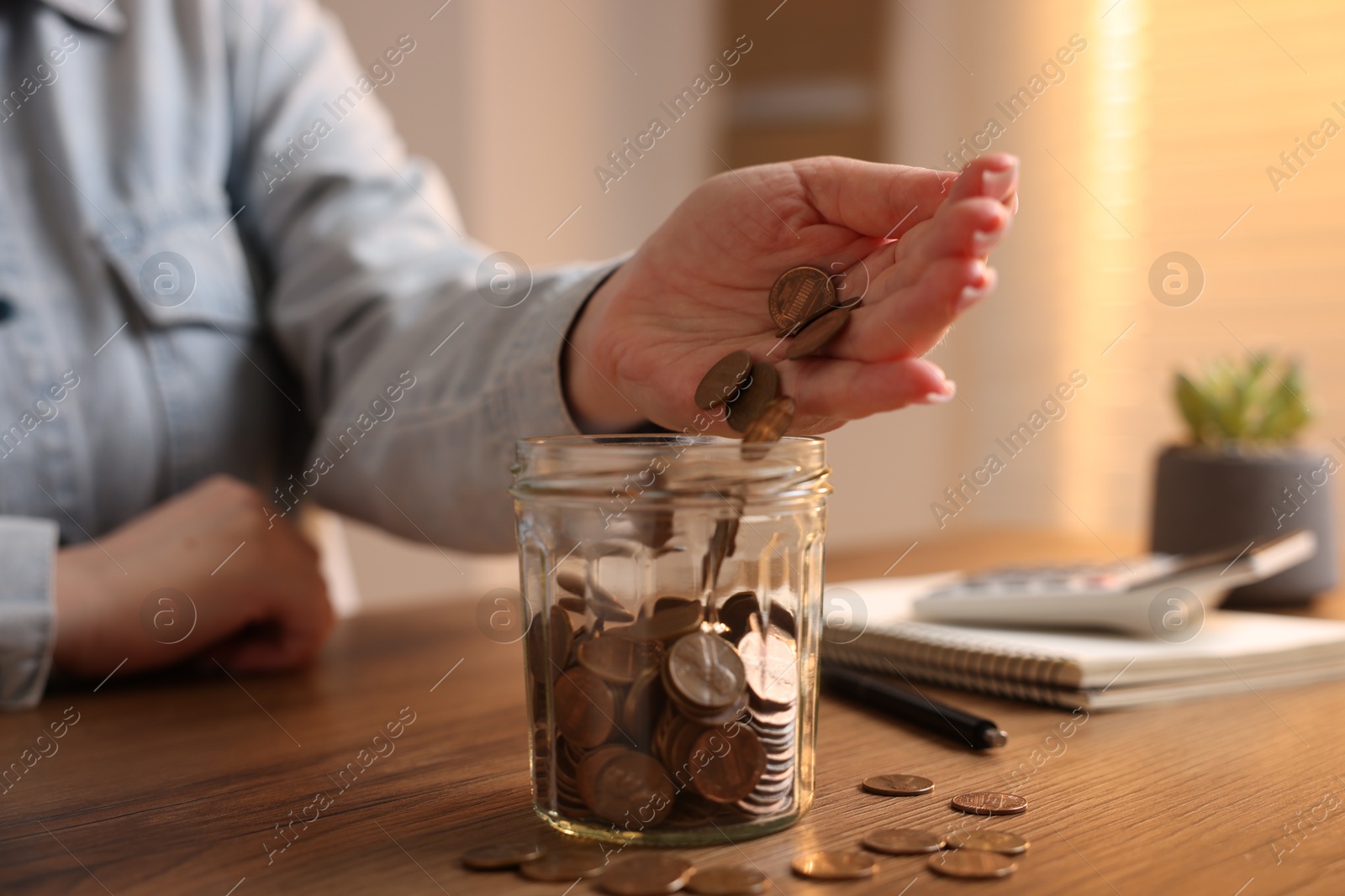 Woman putting coins into jar at wooden table, closeup Photo of Woman putting coins into jar at wooden table, closeup