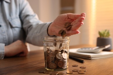 Photo of Woman putting coins into jar at wooden table, closeup