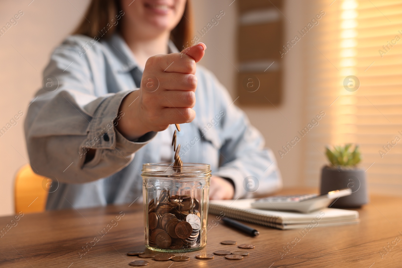 Woman putting coins into jar at wooden table, closeup Photo of Woman putting coins into jar at wooden table, closeup