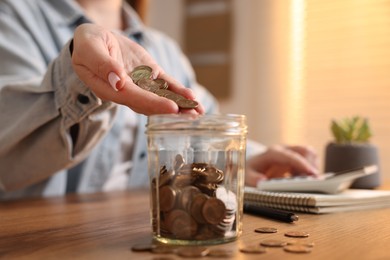 Photo of Woman counting and putting coins into jar at wooden table, closeup