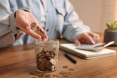 Photo of Woman counting and putting coins into jar at wooden table, closeup