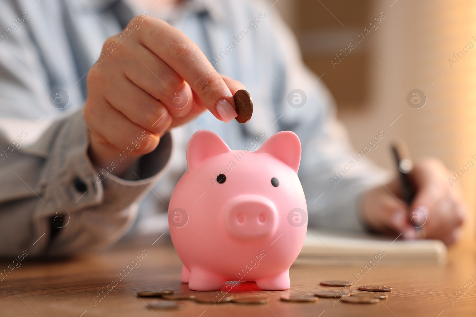 Woman planning budget and putting money into piggybank at wooden table, selective focus Photo of Woman planning budget and putting money into piggybank at wooden table, selective focus