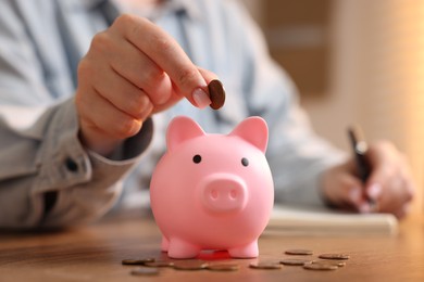 Photo of Woman planning budget and putting money into piggybank at wooden table, selective focus