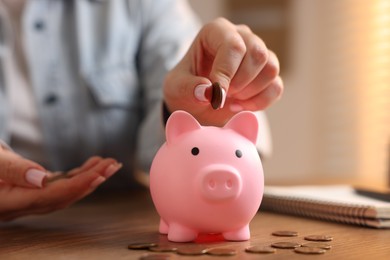 Photo of Woman putting money into piggybank at wooden table, closeup