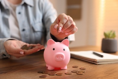 Photo of Woman putting money into piggybank at wooden table, closeup