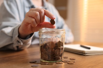 Photo of Woman putting coins into jar at wooden table, selective focus