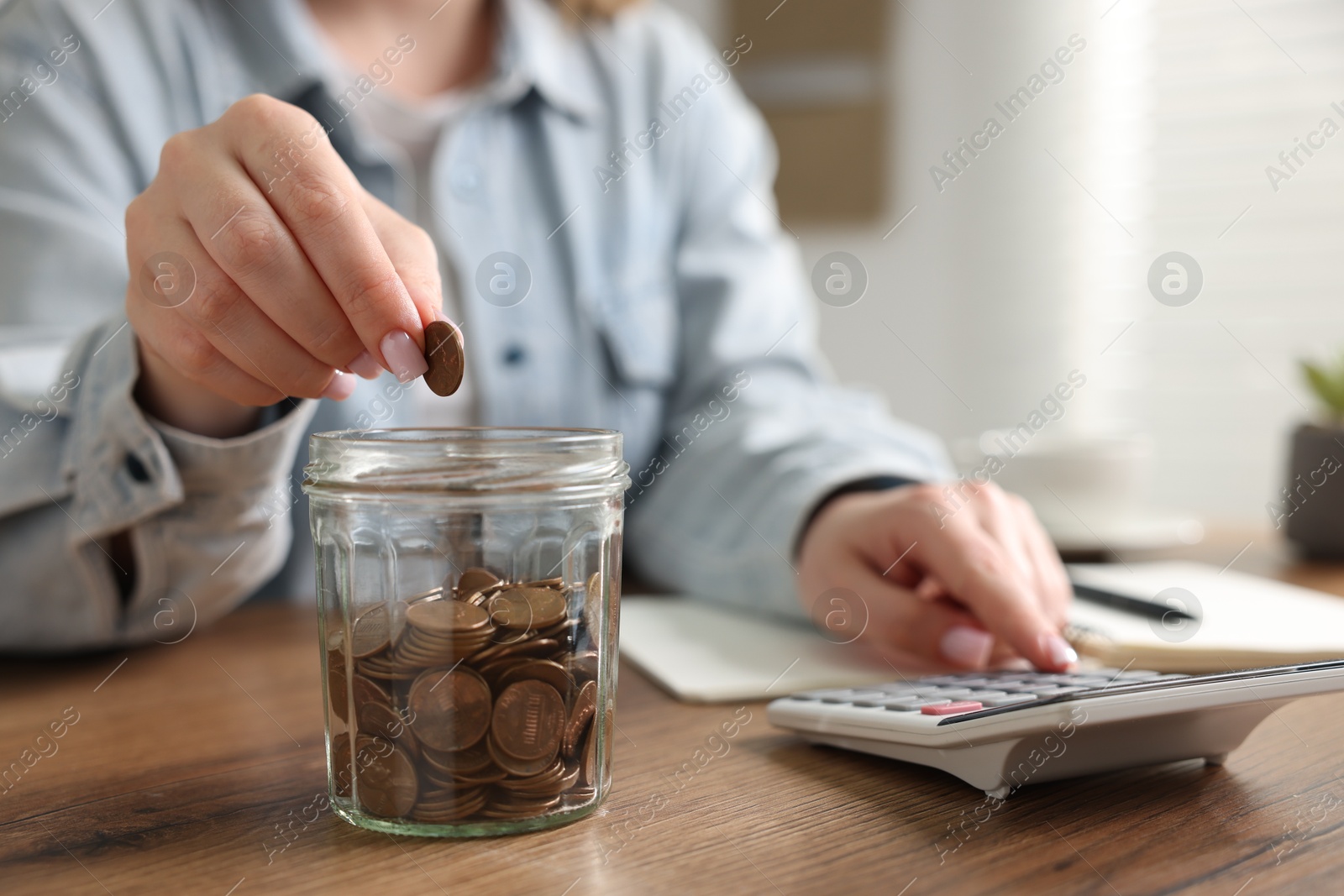 Woman counting and putting coins into jar at wooden table, closeup Photo of Woman counting and putting coins into jar at wooden table, closeup