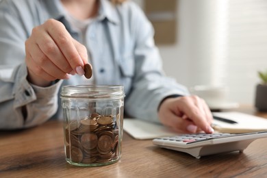 Photo of Woman counting and putting coins into jar at wooden table, closeup